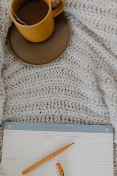 A cozy scene featuring a cup of tea, knitted blanket, and a weekly planner.