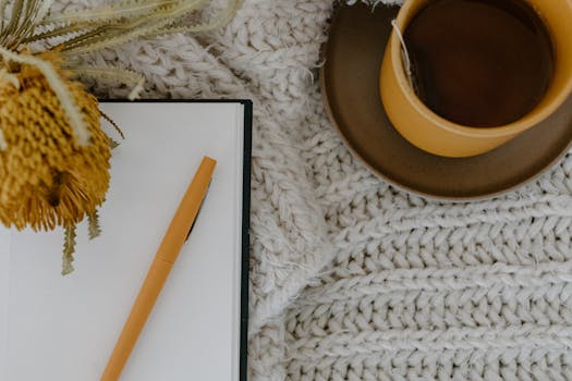 A warm flatlay of herbal tea, notebook, and flower on a knitted blanket.