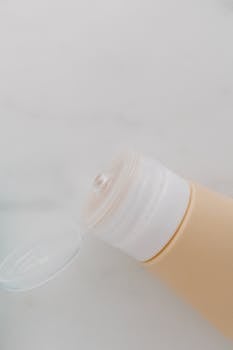 A minimalist close-up of an open lotion tube with cream-colored packaging on a light background.