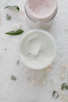 Top view of elegant skincare creams in glass jars with natural elements on a soft white background.