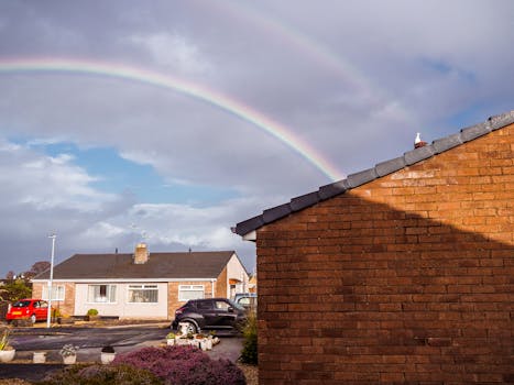 A picturesque view of suburban homes with a stunning double rainbow overhead, creating a serene urban scene.