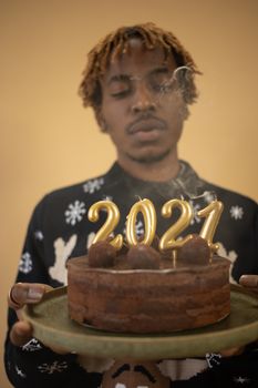 A man holds a chocolate cake with 2021 candles, signifying New Year celebration.