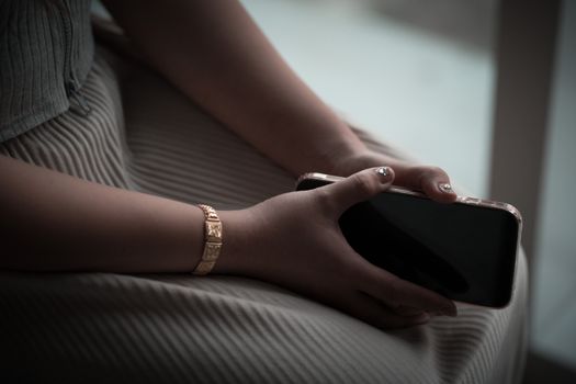 Close-up of a woman's hands holding a smartphone, displaying a golden bracelet.