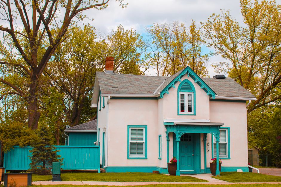 A charming historical house with vibrant blue accents surrounded by trees under a cloudy sky.