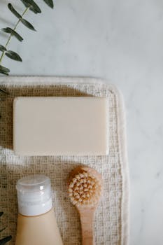Overhead view of soap, bottle, and brush on a textured towel with plants, perfect for beauty product backgrounds.