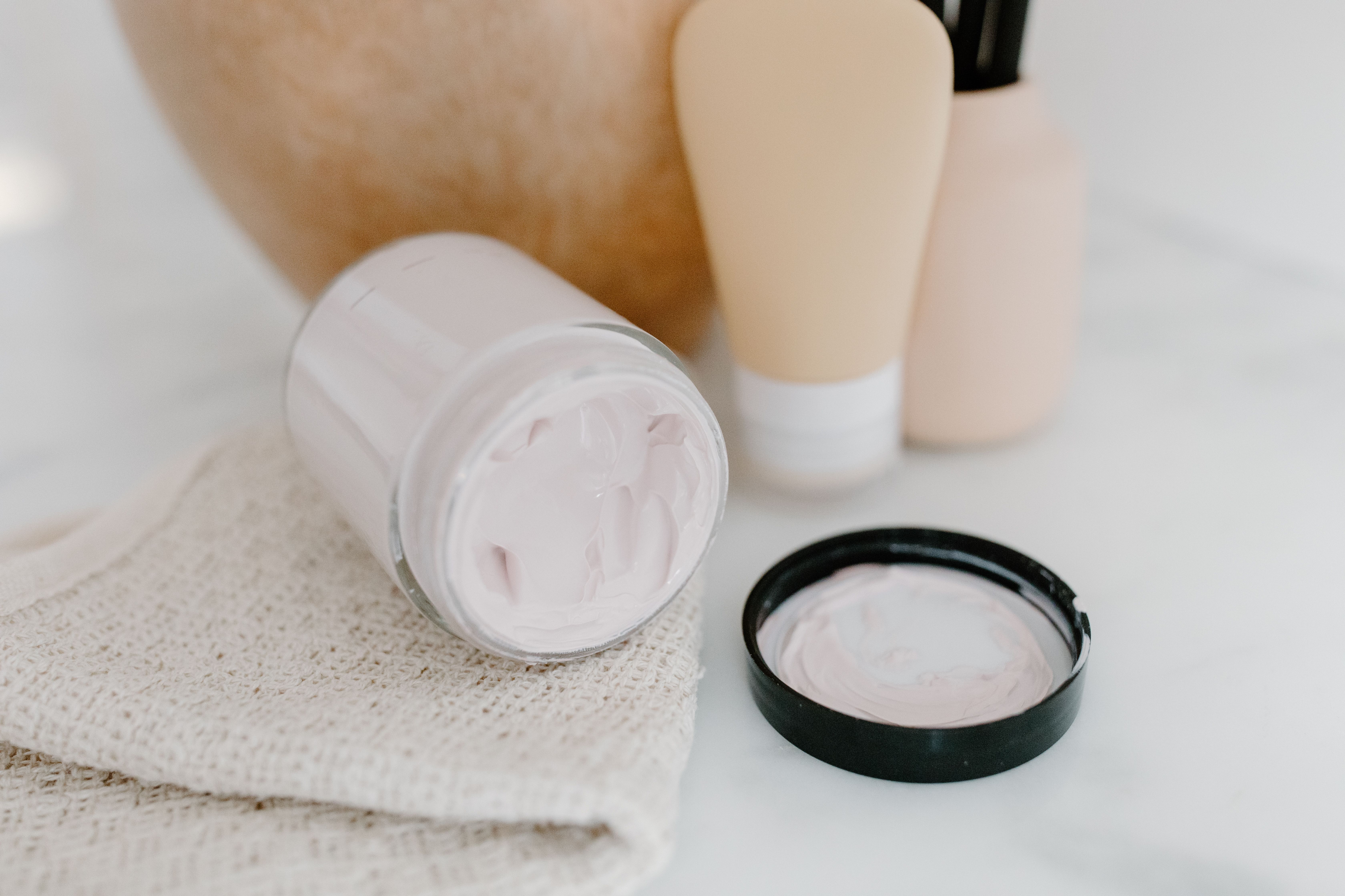 Glass jar of face cream surrounded by gentle skincare products on a neutral background