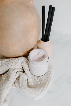 A minimalist arrangement featuring a cream jar, ceramic vase, and towels, ideal for a beauty product display.