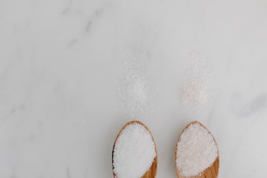Two wooden spoons filled with salt placed on a white marble surface with ample copy space.