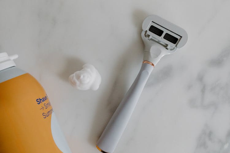 A Handheld Shaver On Marble Surface Beside Shaving Foam 