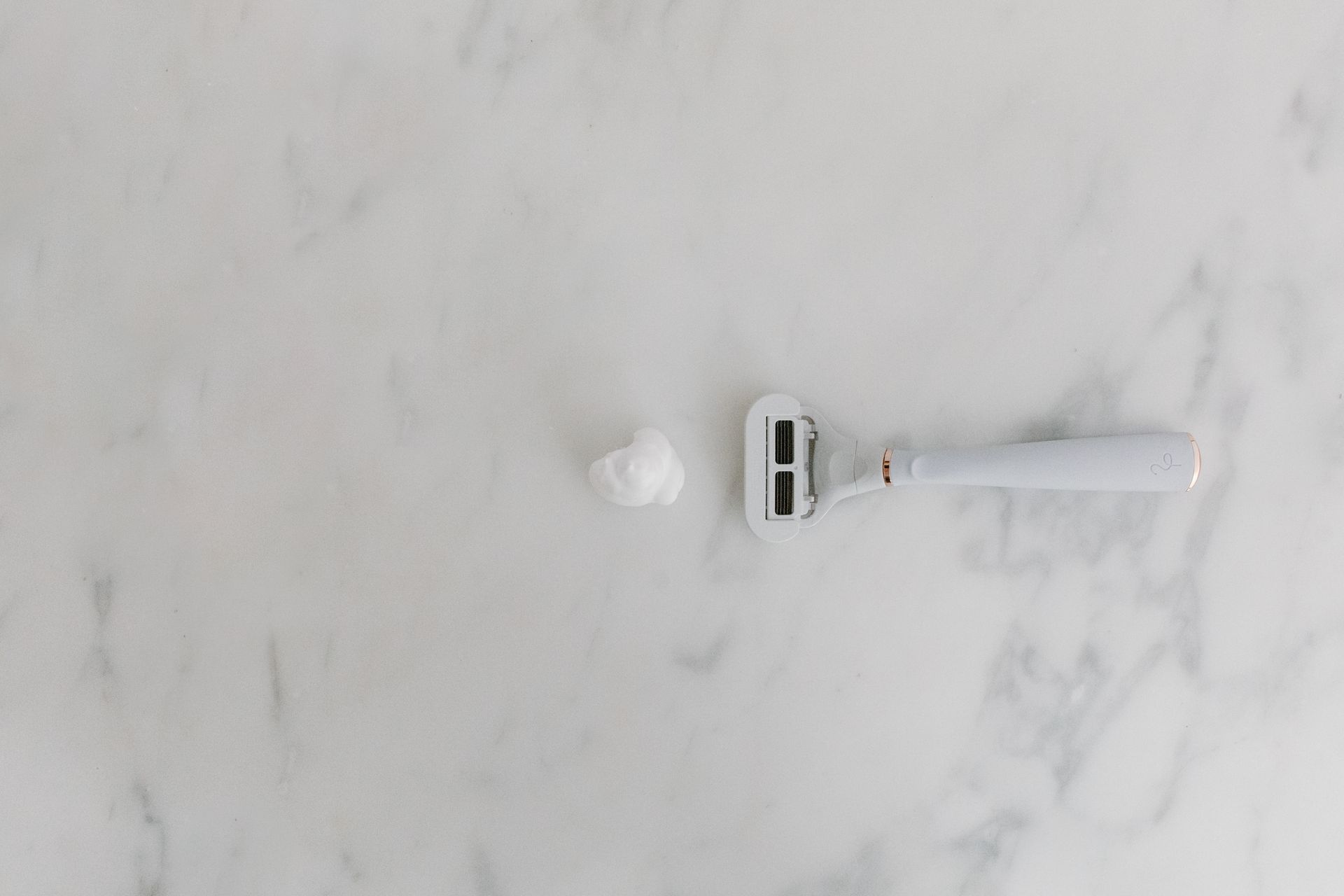 A White Shaver and Shaving Foam on Marble Surface