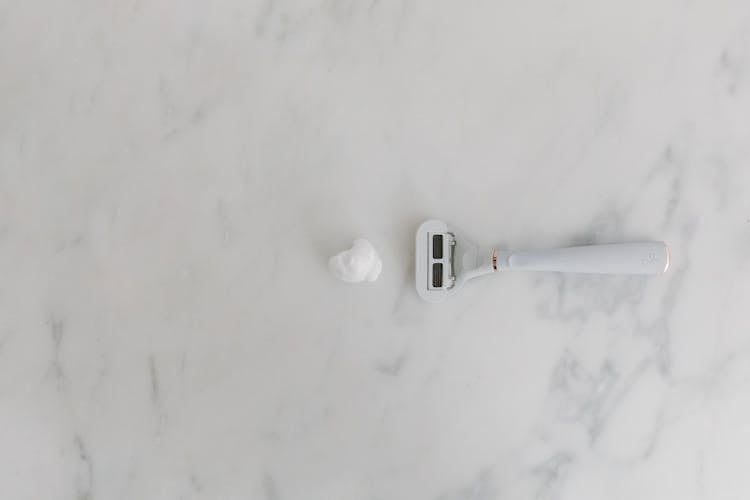 A White Shaver And Shaving Foam On Marble Surface