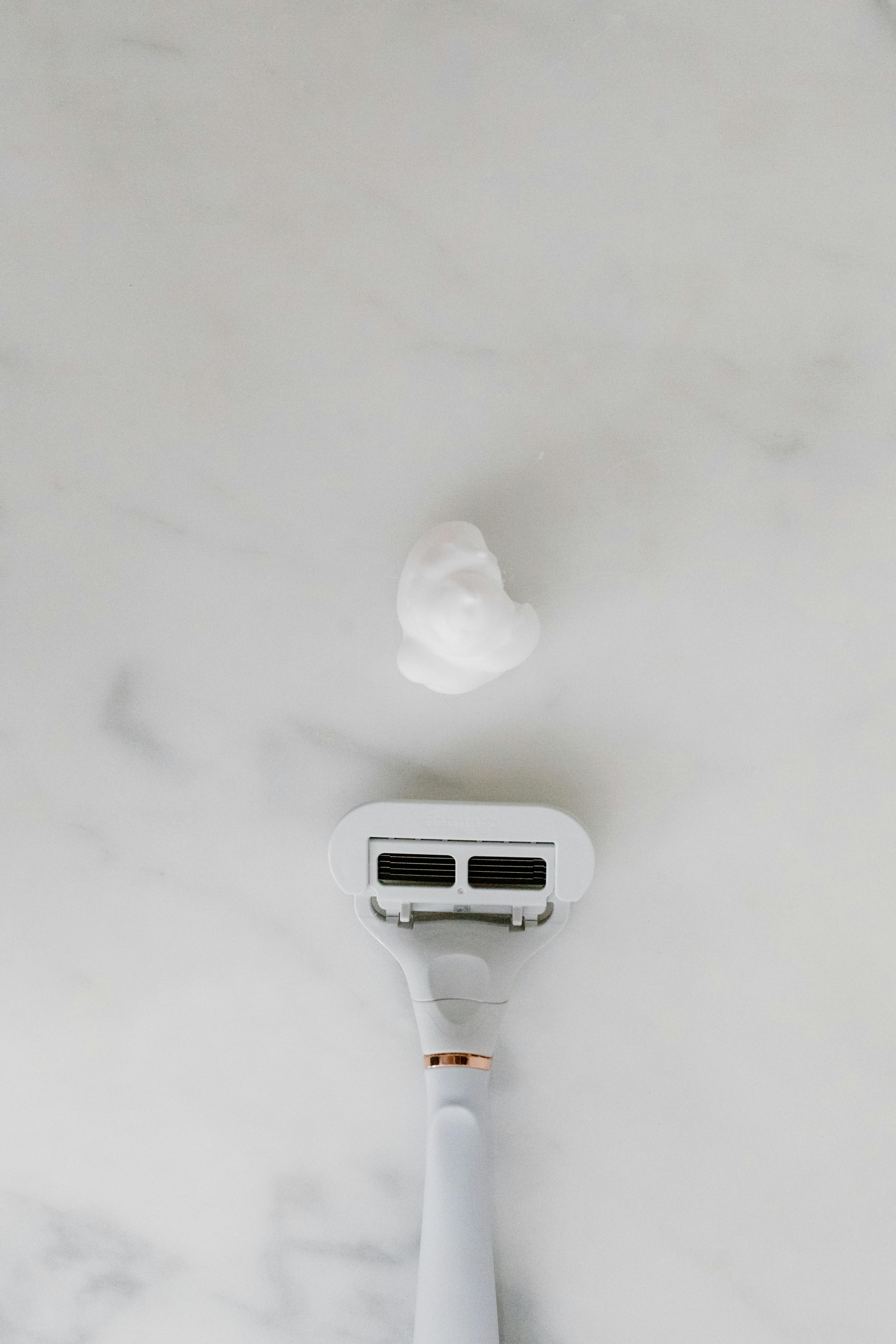 Top view of a shaving razor and foam on a light surface, emphasizing grooming essentials.