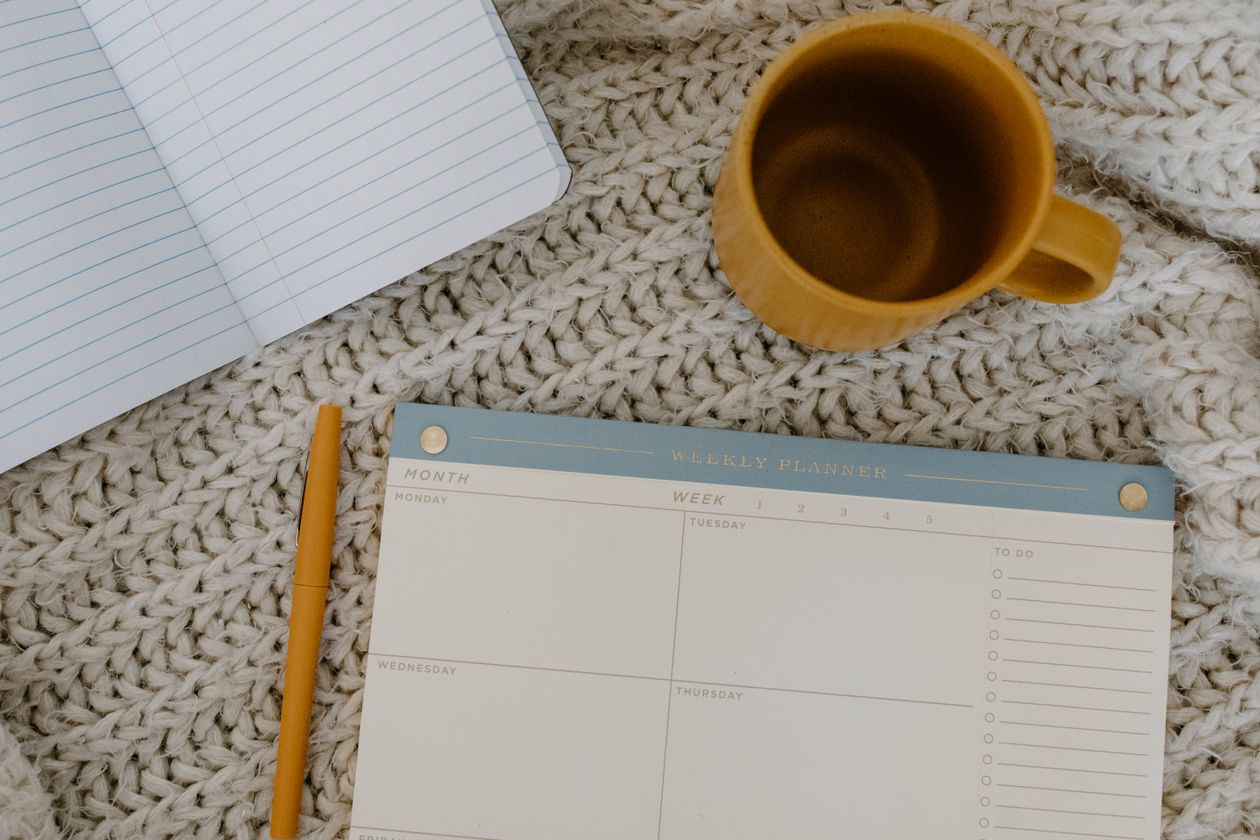 A weekly planner, a notebook and a mug of coffee on a knitted blanket