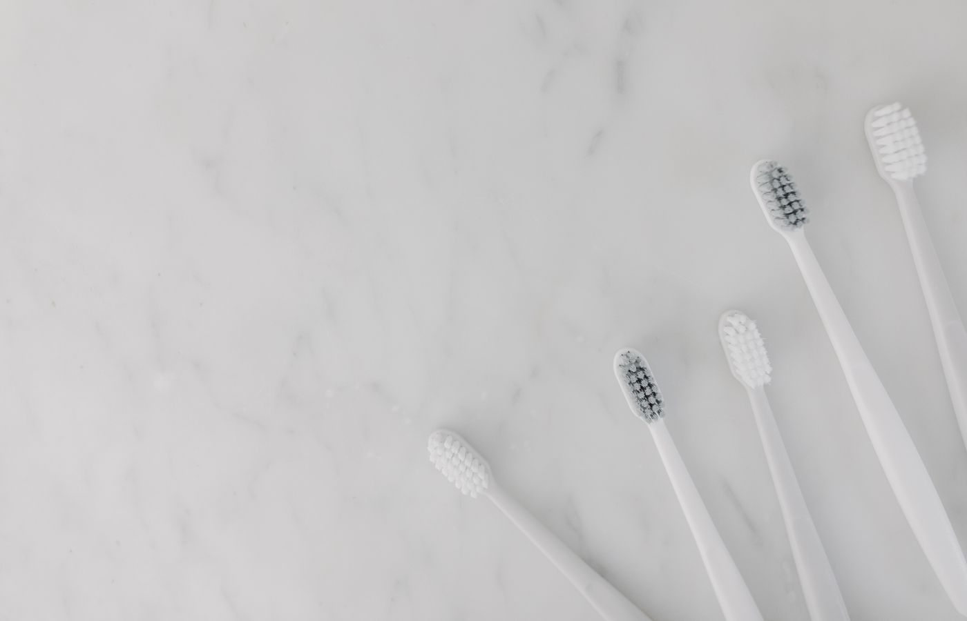 Elegant display of white toothbrushes on a marble surface, emphasizing hygiene and simplicity.