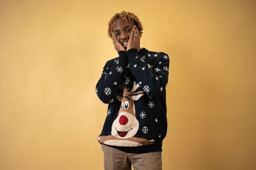 Free A young man smiling in a festive reindeer sweater against a warm yellow background. Stock Photo