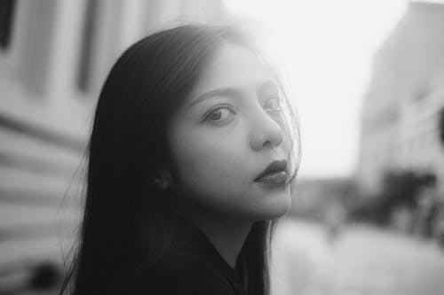 Black and white side view of young ethnic female looking at camera in town in daylight