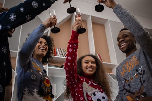 Free Group of friends in festive sweaters cheering with champagne indoors. Stock Photo