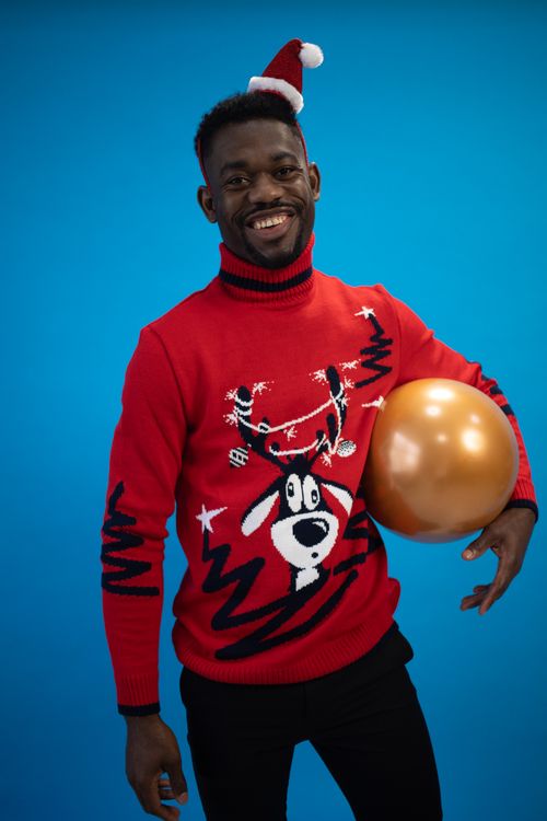 Free Smiling African American man wearing a red Christmas sweater and Santa hat, holding a gold balloon. Stock Photo