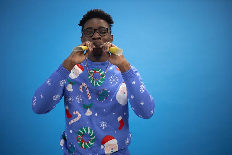 A Man Wearing An Ugly Christmas Sweater Blowing Paper Trumpets