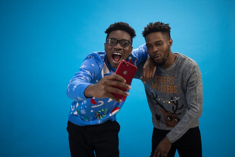 A Pair Of Men Wearing An Ugly Christmas Sweaters Taking Selfie