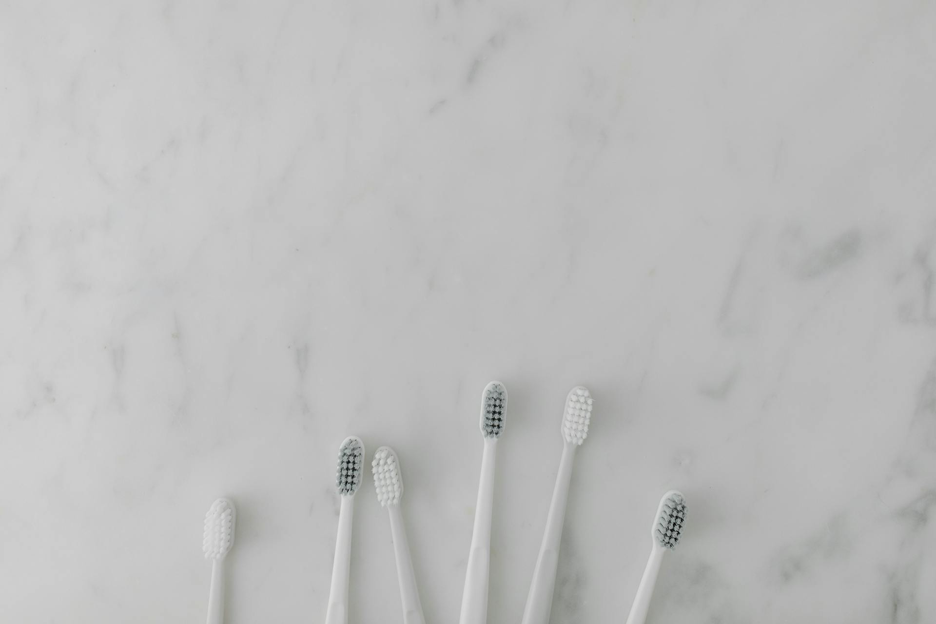 Five minimalist toothbrushes arranged on a marble surface, perfect for dental care themes.