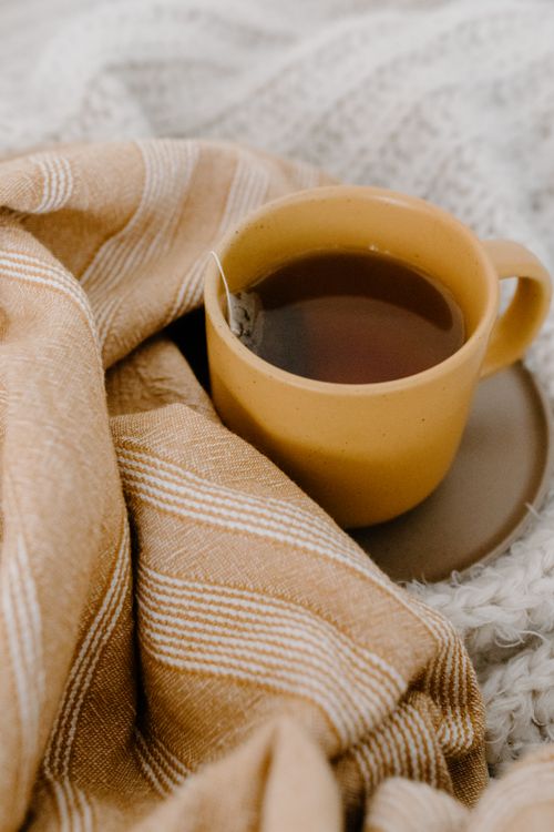Free Yellow cup of tea with a teabag nestled in warm, patterned textiles portraying a cozy atmosphere. Stock Photo