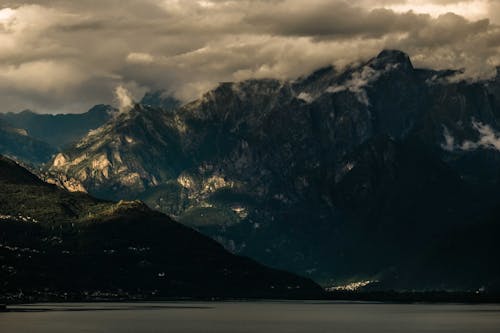 Thick clouds floating over lake surrounded by rocky mountains