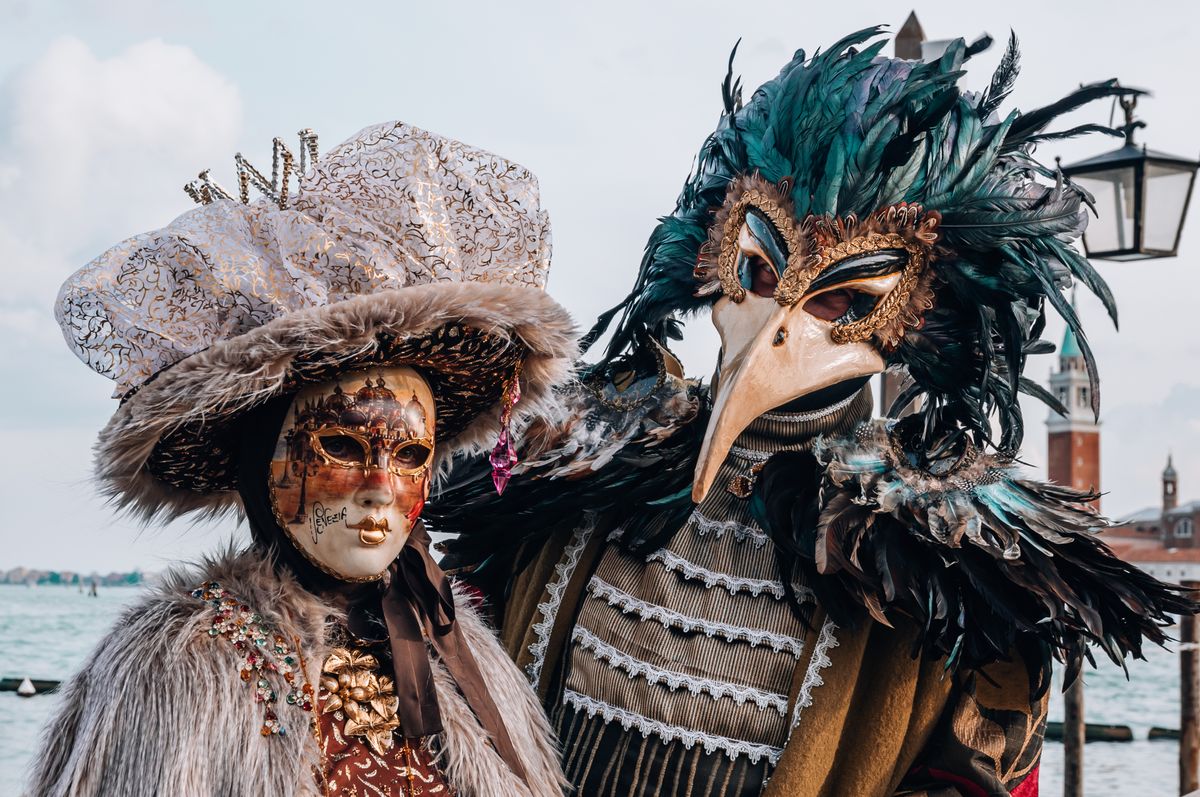 Masked figures in costume at the Venice Carnival, the lagoon and San Giorgio behind them