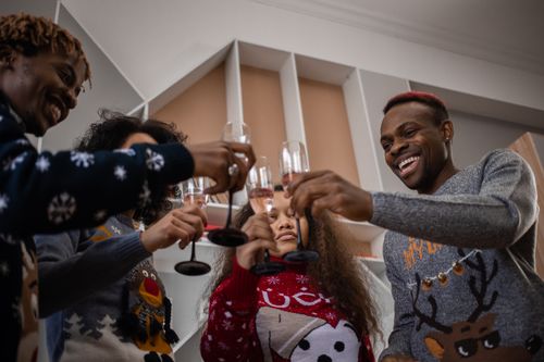 Free A joyful group of friends celebrating indoors wearing festive holiday sweaters and toasting with wine glasses. Stock Photo