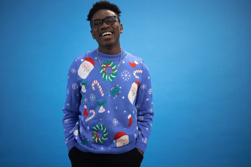 Free A cheerful man wearing a festive Christmas sweater poses against a vibrant blue backdrop. Stock Photo