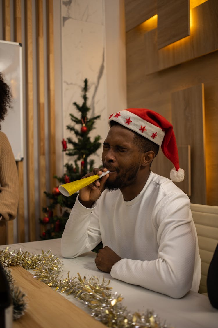 A Man Wearing A Santa Hat Blowing A Paper Trumpet