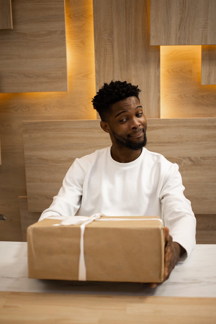 Photo Of A Man In A White Sweatshirt Holding A Brown Gift Box