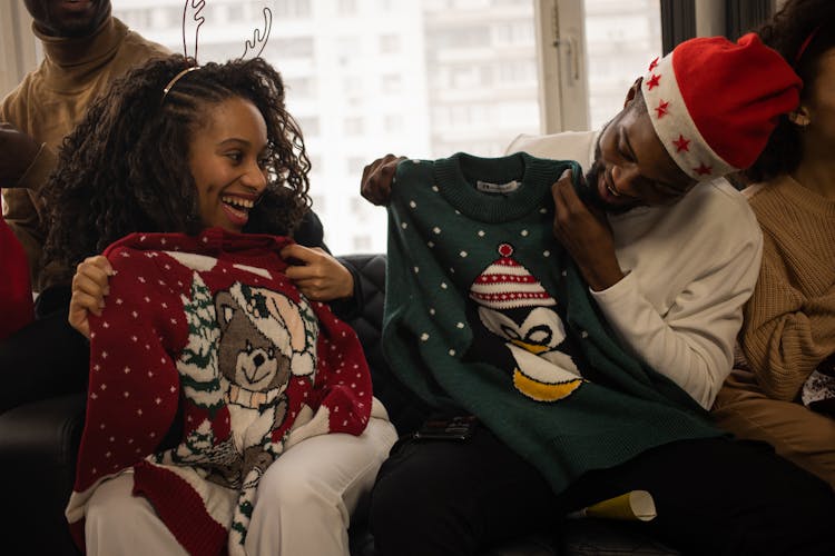 Man And Woman Celebrating Christmas And Looking At Their Christmas Sweaters Laughing 