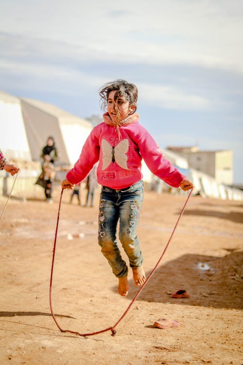 Free Full body of little barefoot girl near settlement with tents and people on blurred background Stock Photo
