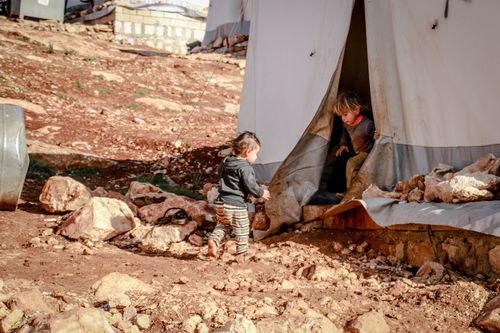 Free Little poor kids playing among tents of settlement on rough ground in daytime Stock Photo