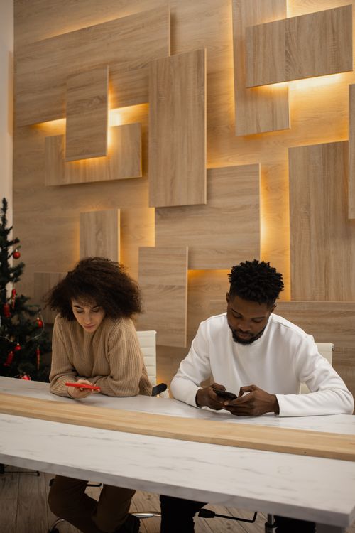 Free Two people using mobile phones at a stylish indoor setting with modern wood panel decor. Stock Photo