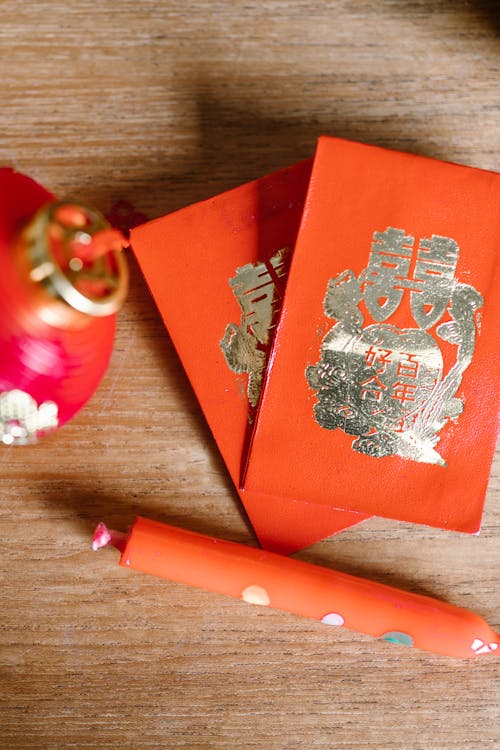 Close-up of Lunar New Year red envelopes and a decorative candle, arranged on a wooden surface with a festive red lantern in the background