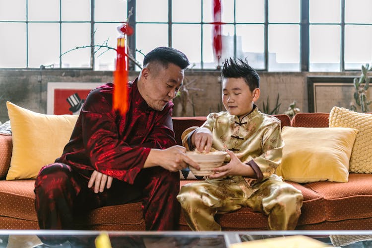 Father And Son Sitting On Red Sofa