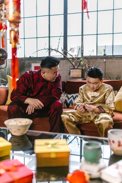 Father and Son Wearing Traditional Clothing Sitting on a Couch while Having a Conversation