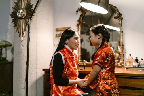 Free A mother and daughter in traditional Chinese clothing, smiling and holding hands indoors. Stock Photo