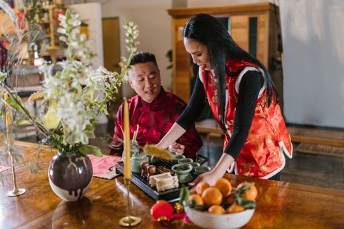 Free A couple dressed in traditional attire enjoying a tea ceremony with a decorative table setup indoors. Stock Photo