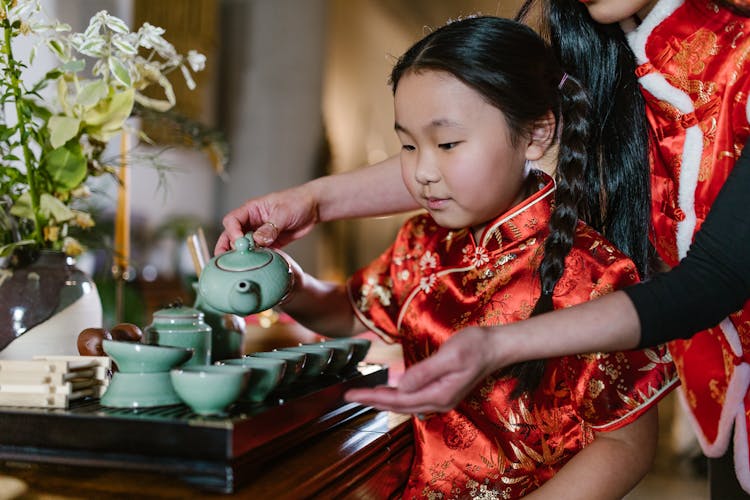 
A Mother Teaching Her Daughter On How To Pour Tea