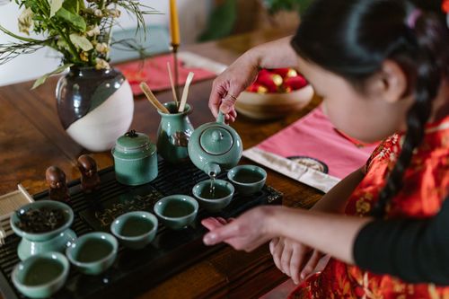 Free A young girl in traditional attire pours tea in a serene indoor setting. Stock Photo