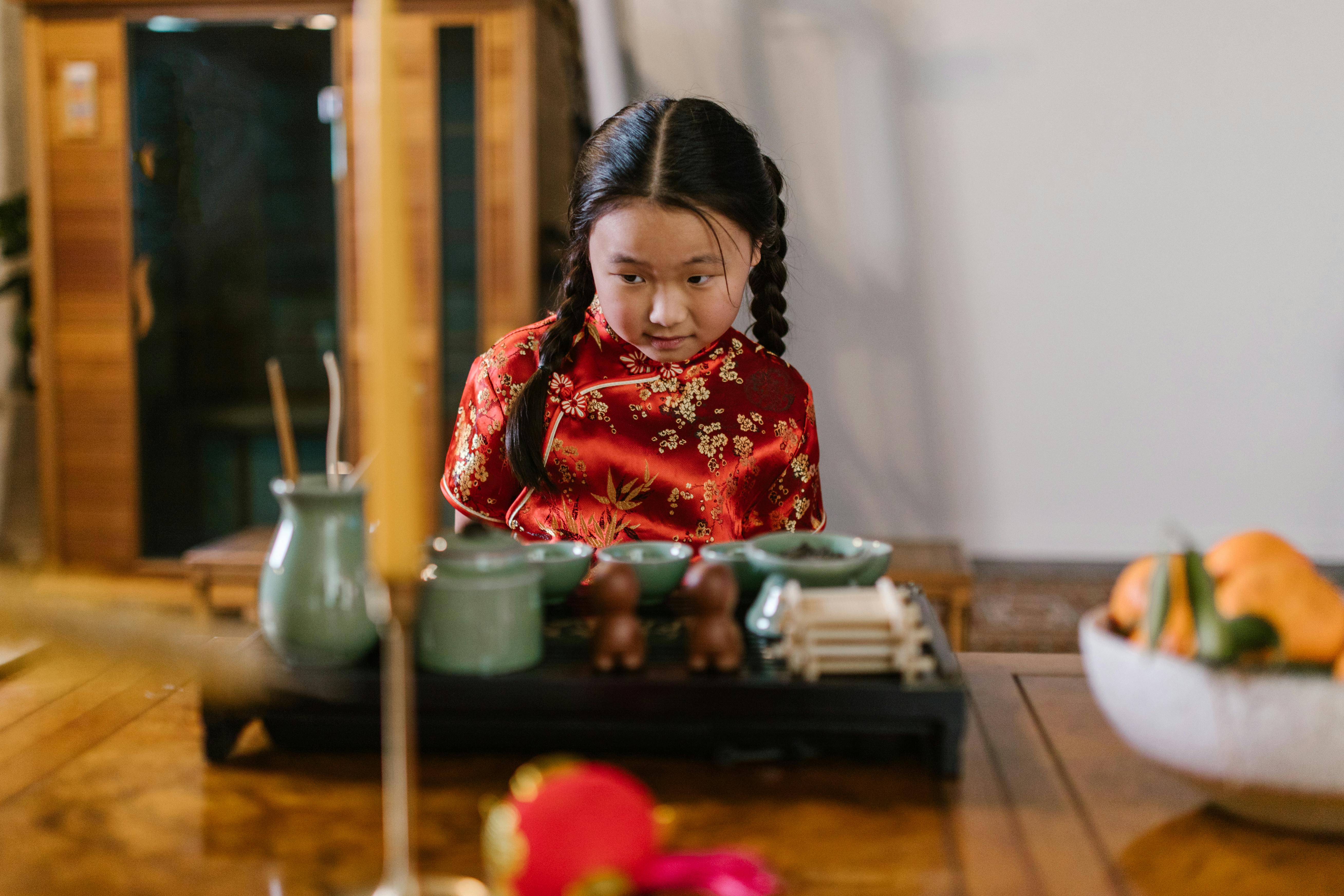 A child wearing a red cheongsam sits at a table with traditional Chinese decor.
