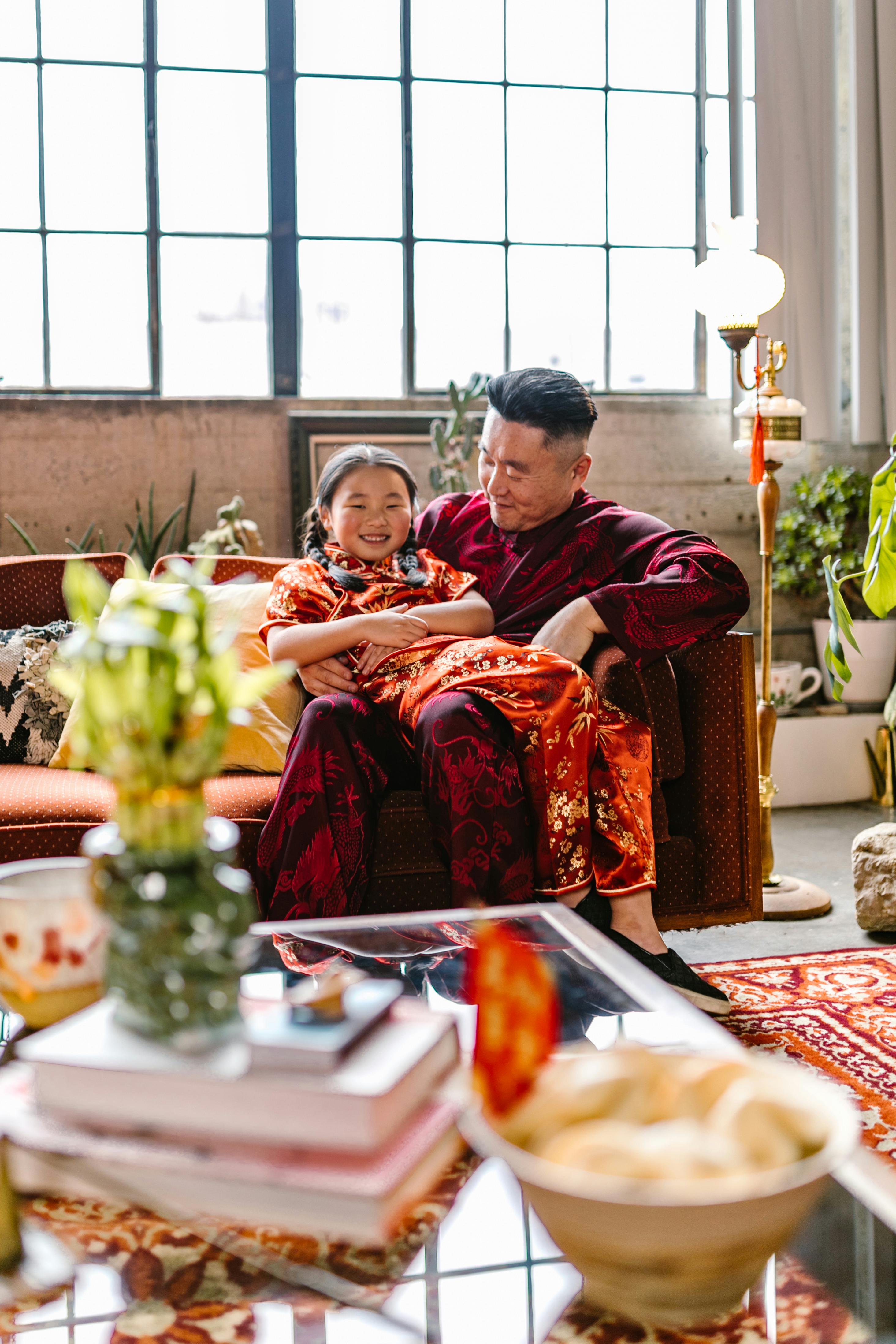 Father and daughter bonding on a couch in traditional clothing, with a warm, cozy ambiance.