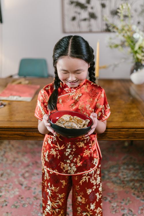 Free Smiling girl in traditional Chinese dress holding a bowl of dumplings indoors. Stock Photo