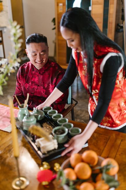 A couple engaged in a traditional tea ceremony wearing vibrant cultural clothing indoors.