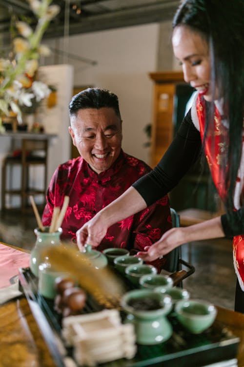 Woman Preparing Tea Next to a Man in Red Shirt