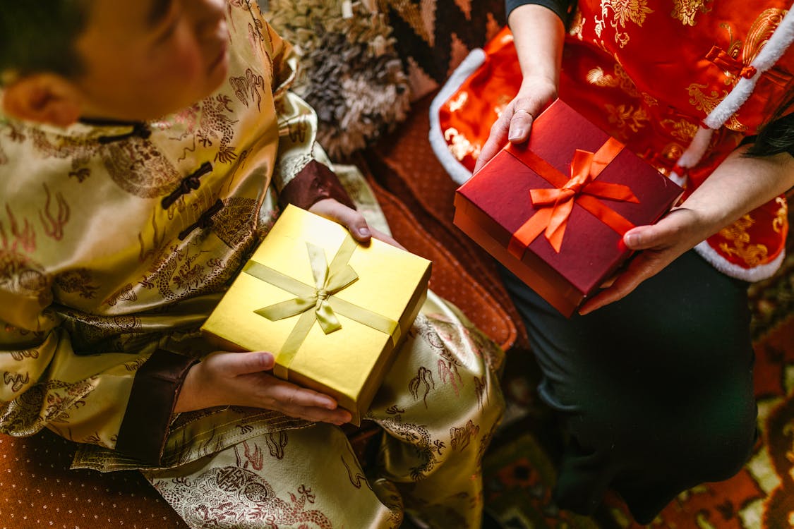 Two children in traditional East Asian garments exchanging brightly wrapped gifts