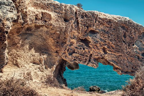 Free A breathtaking natural rock arch frames a clear blue sea under a vibrant summer sky. Stock Photo